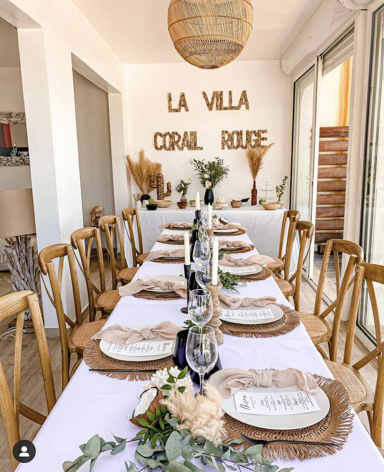 Une table à manger agrémentée de chaises en bois, d’une nappe blanche et de décorations centrales comprenant des bougies et des éléments de verdure.