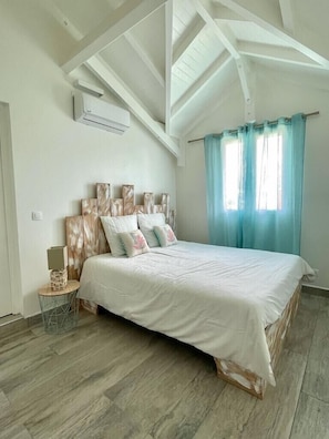 Une chambre à coucher avec un grand lit, une tête de lit en bois, une petite table de chevet et une fenêtre avec des rideaux.