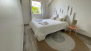 A bedroom with a bed, a window, a bedside table, and a rug. - Red coral, feet in the sand (Saint-François)