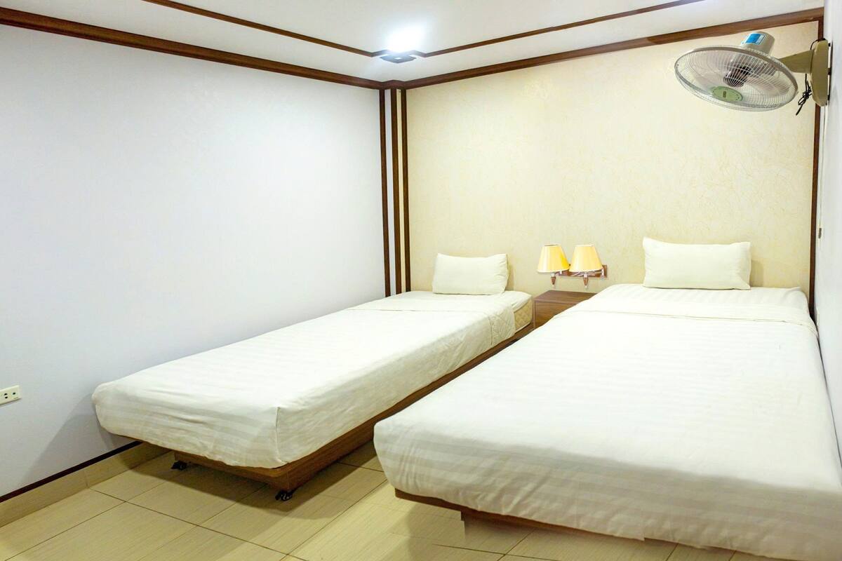 A hotel room with two single beds, a wall-mounted fan, and two bedside lamps.