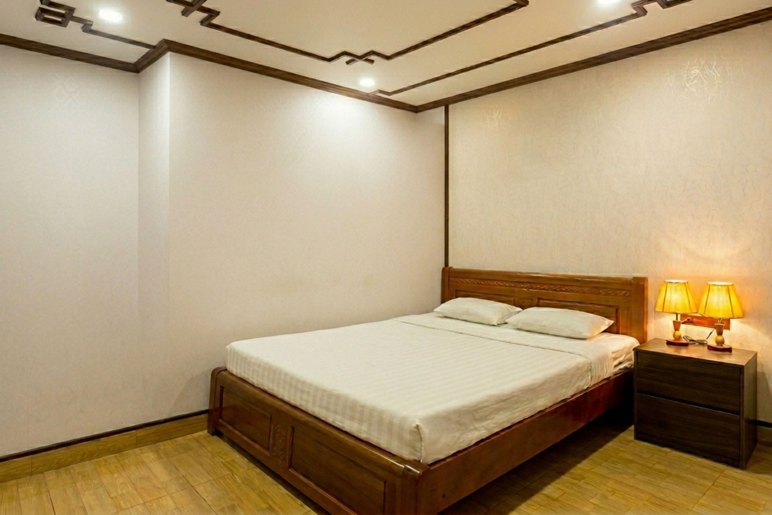 A bedroom with a wooden bed, a nightstand with a lamp, and a plain wall.