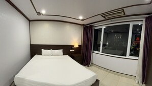 A hotel room with a large bed, a nightstand with a lamp, a window with curtains, and a view of the city at night. - Anh Duong Hotel (Hanoi)