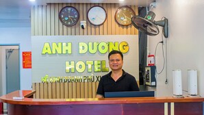 A hotel reception desk with a wooden panel wall, multiple clocks, and a fan. - Anh Duong Hotel (Hanoi)