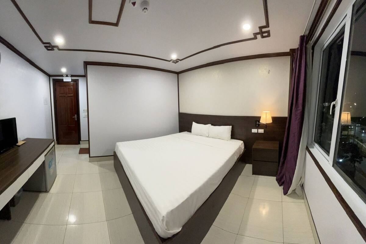 A hotel room with a bed, a TV, a nightstand, a window, and a door.