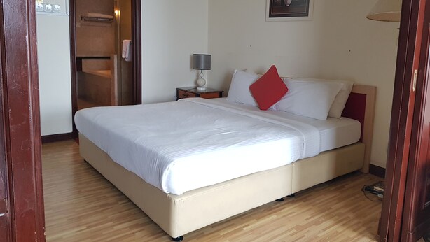 A bedroom with a bed, a nightstand, a lamp, a door, and a wall-mounted picture.