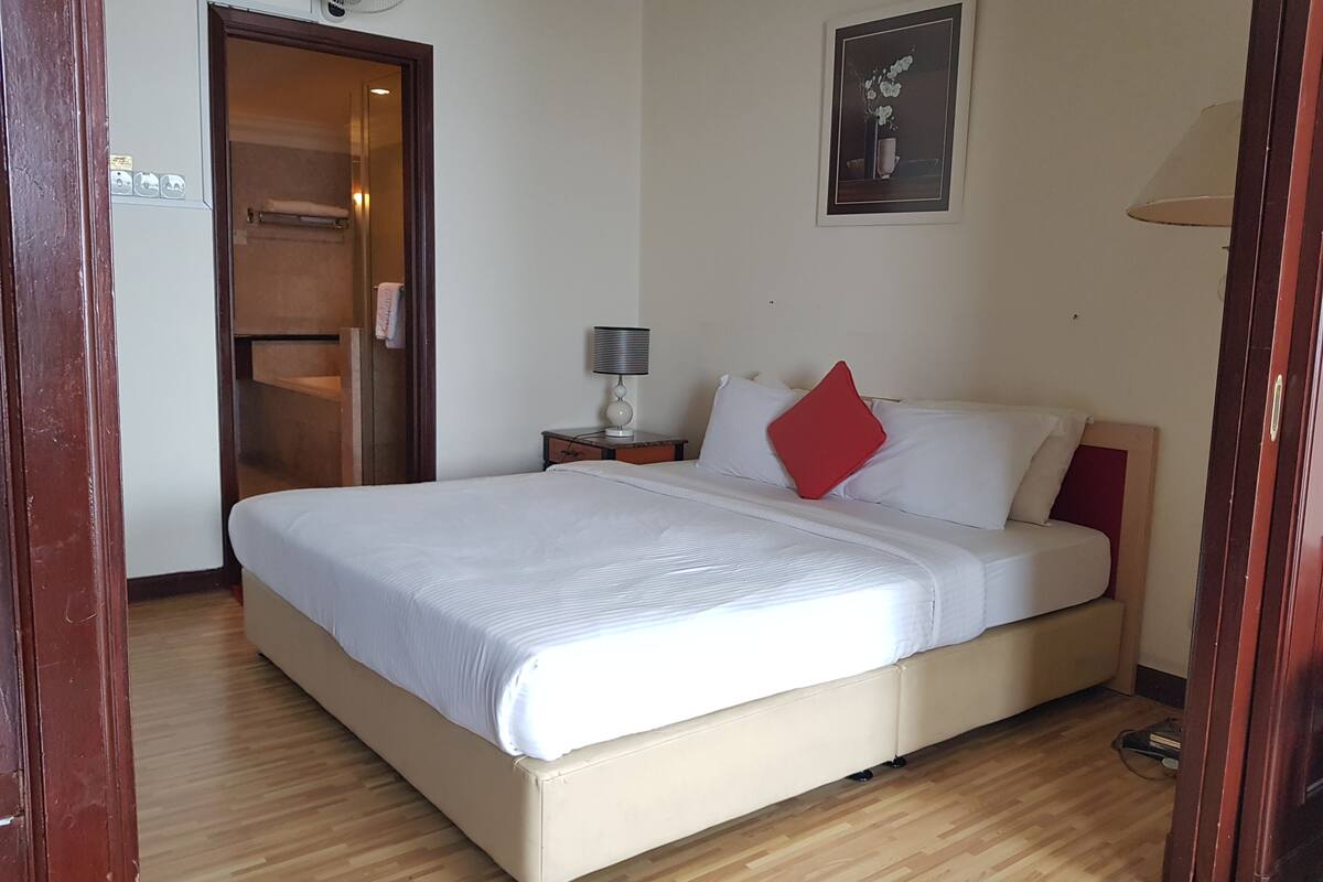 A bedroom with a bed, a nightstand, a lamp, a door, and a wall-mounted picture.