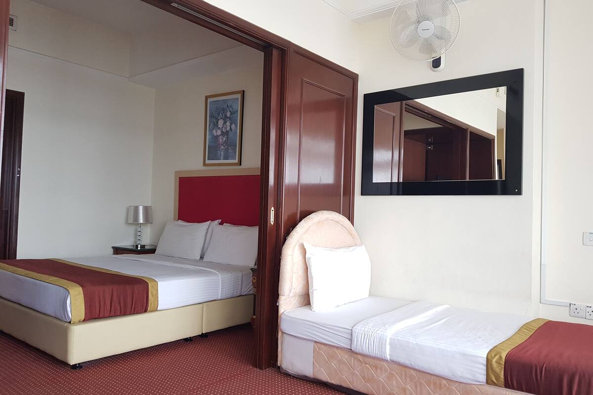 A hotel room with two beds, a red headboard, a bedside lamp, a mirror, and a wall-mounted fan.