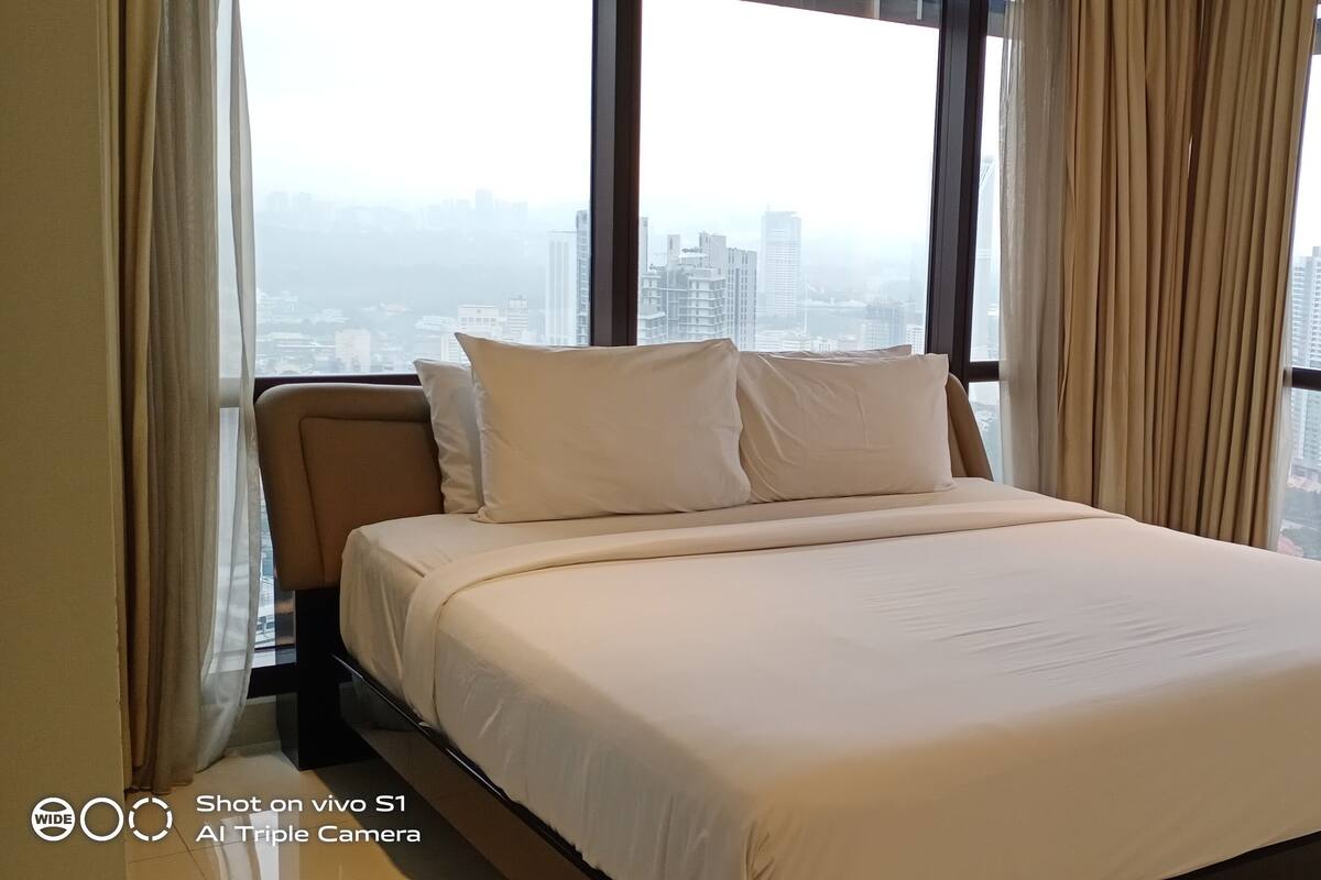 A modern bedroom with a large bed, a view of a cityscape through floor-to-ceiling windows, and a city view from the window.