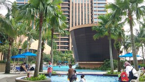 A hotel with a swimming pool surrounded by palm trees and lounge chairs.