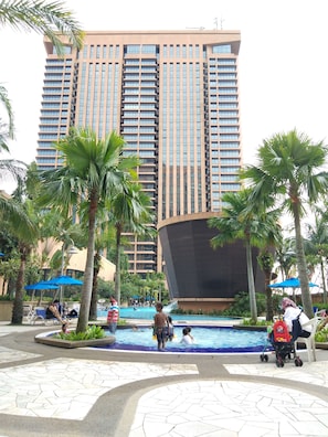 Un hotel con piscina circondata da palme e lettini da relax.