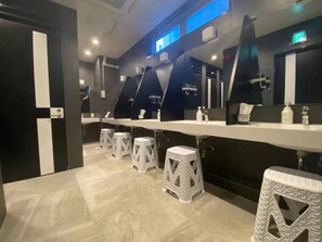 A modern bathroom with multiple sinks, white stools, and a black and white color scheme. - Capsule Hotel 2nd BOX (Naha)