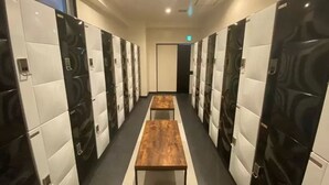 A hotel corridor with lockers on both sides, a central bench, and a door at the end. - Capsule Hotel 2nd BOX (Naha)