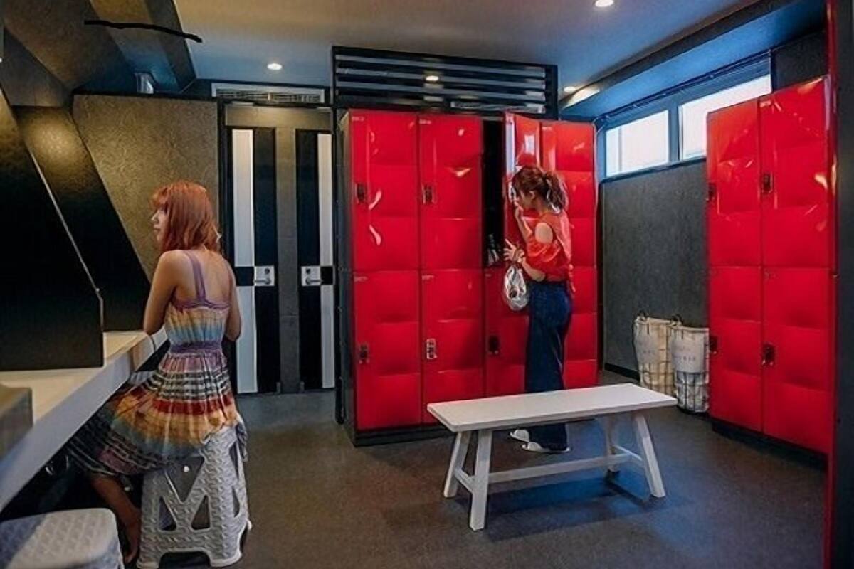 A room with red lockers, a bench, and a person sitting at a table.