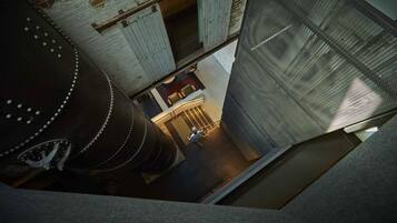A high-angle view of a building's interior with a large cylindrical tank, a staircase, and a mesh-covered wall.