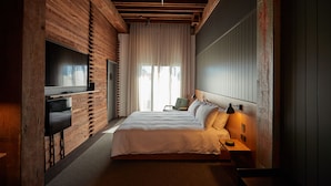 A bedroom with a large bed, a TV mounted on the wall, a chair, and a bedside table with a lamp. - Premier Mill Hotel (Katanning)
