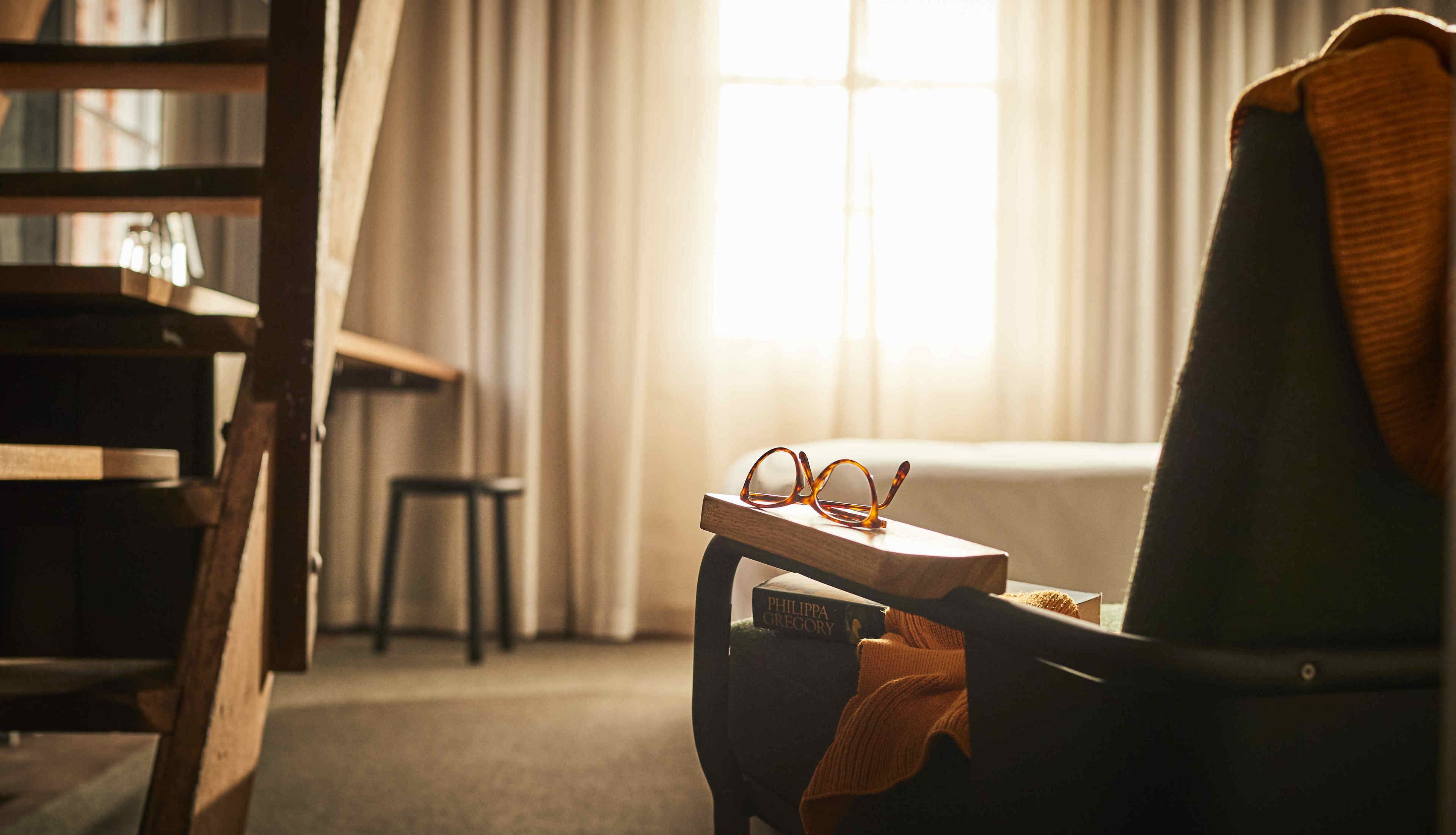 Un rincón acogedor para leer, con un sillón, una mesita y un par de gafas.