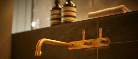 A bathroom with a single gold-colored faucet mounted on a dark tiled wall.