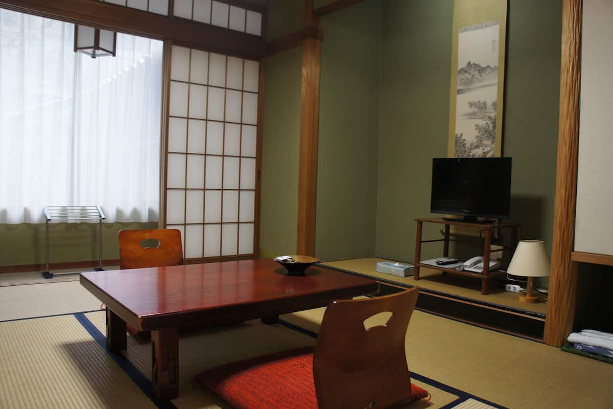 A traditional Japanese room with tatami flooring, a low table, and a television on a wooden stand.