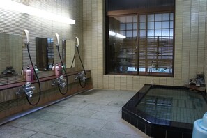 A bathroom with a large mirror, a bathtub, and a window with blinds.