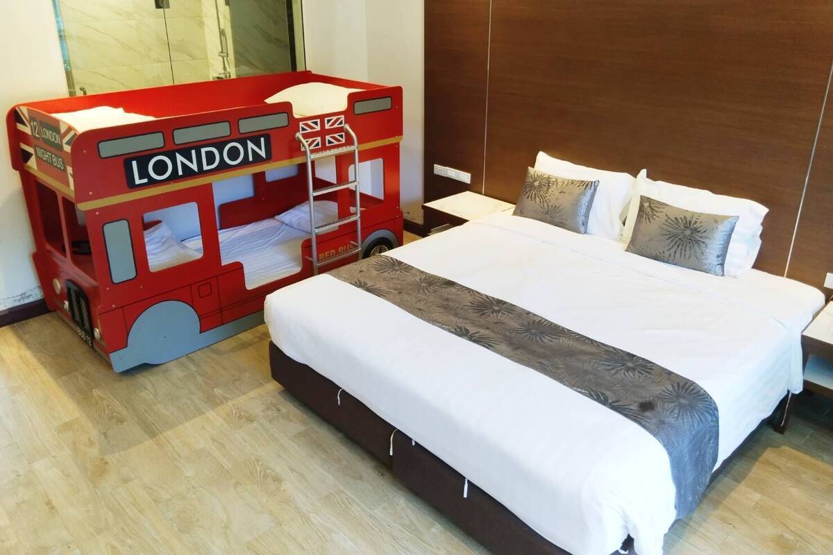 Een hotelkamer met een groot bed, een houten hoofdeinde en een bed in de vorm van een rode dubbeldekkerbus.