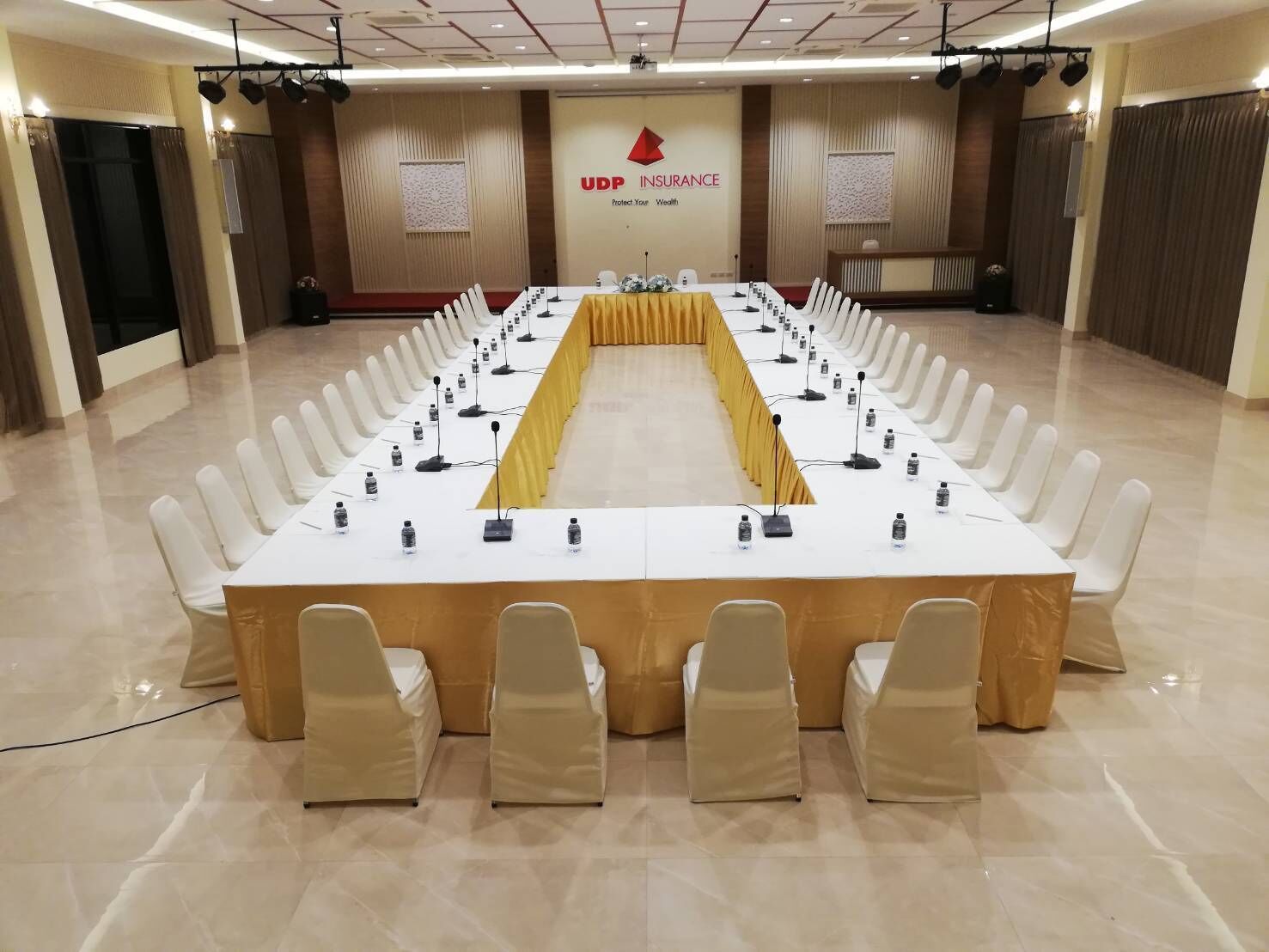 Een vergaderzaal met een lange tafel, witte stoelen en een geel tafelkleed.