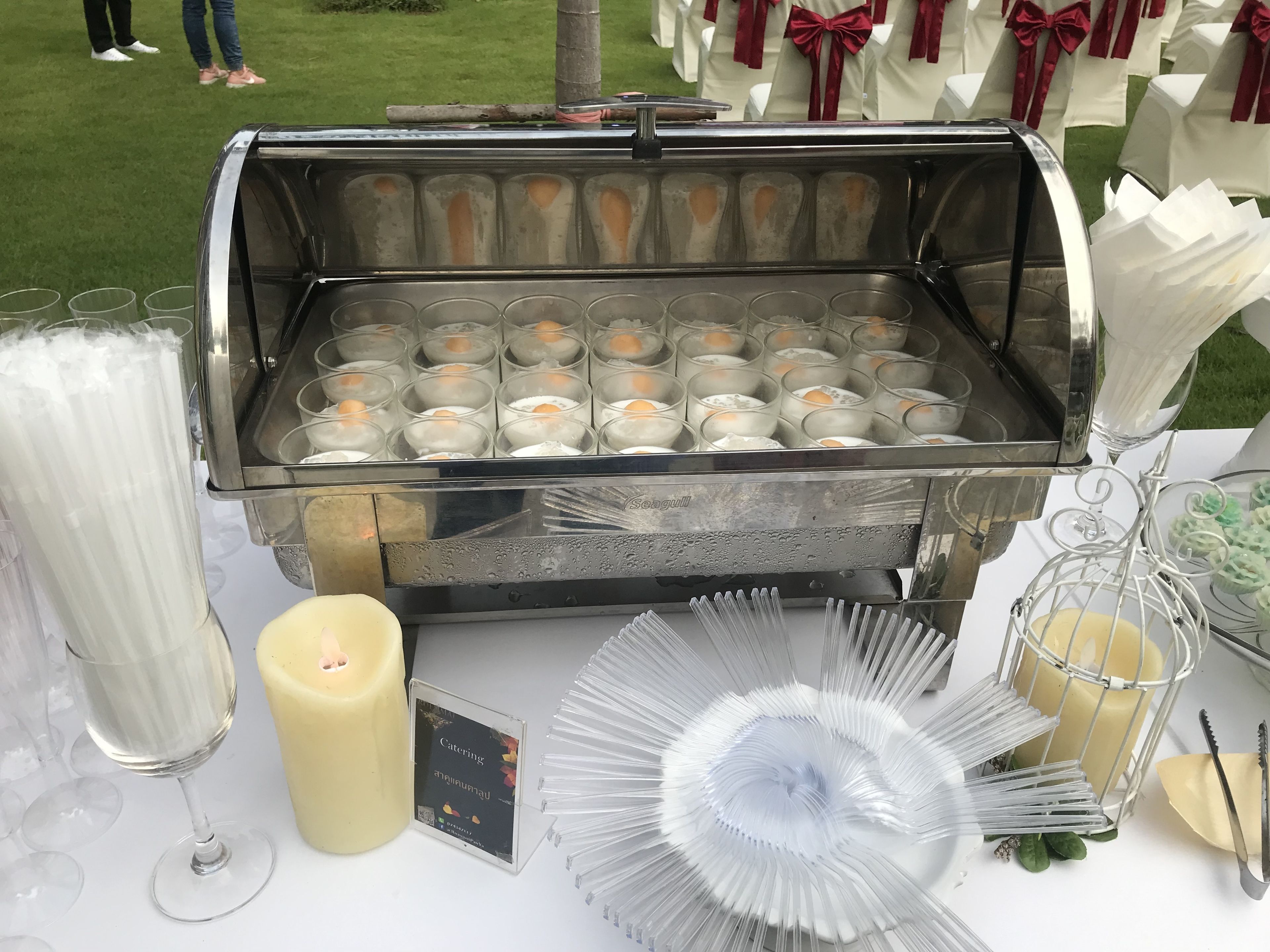 A buffet setup with multiple drink dispensers, a candle, and a sign indicating catering services.