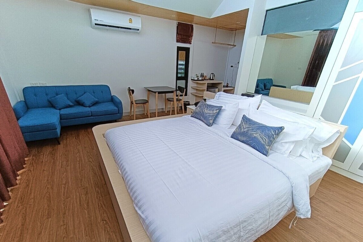 Een moderne slaapkamer met een groot bed, een blauwe bank, een klein tafeltje en een spiegel.