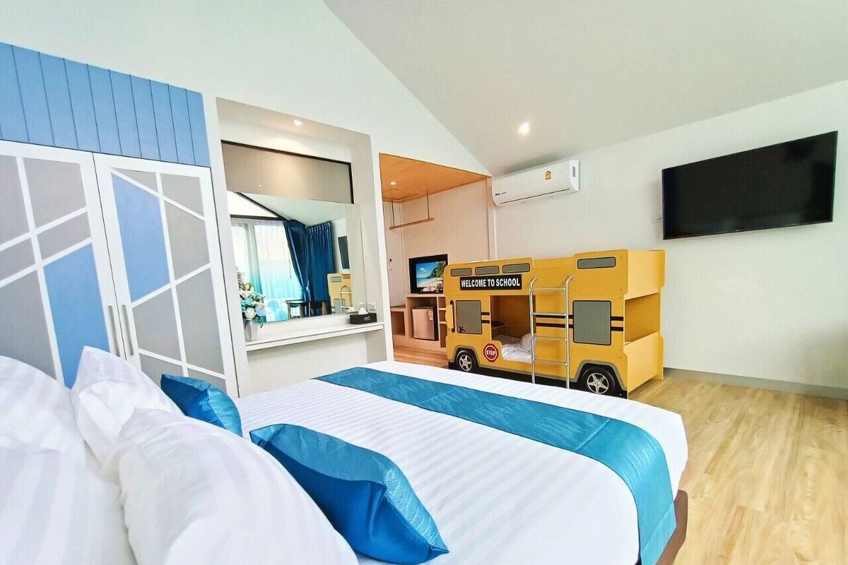 Hotelkamer met een bed, een televisie, een wandairconditioner en een kinderspeelruimte met een gele bus.