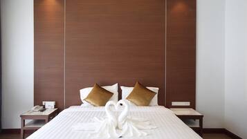 Habitación de hotel con una cama grande, dos almohadas, una mesita de noche con teléfono y una decoración de toallas en forma de cisne sobre la cama.