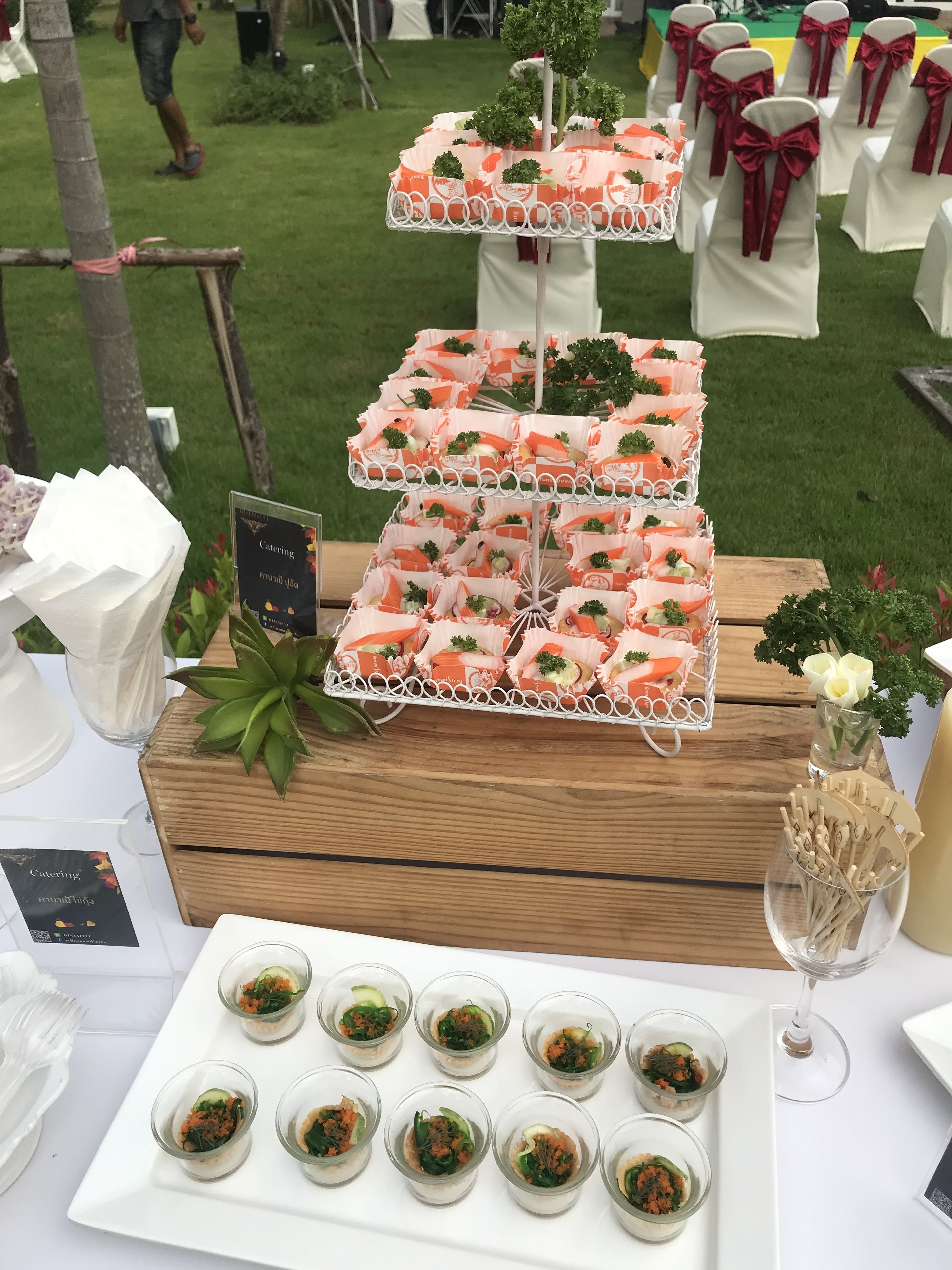 A buffet table with neatly arranged food items, including a three-tiered display of appetizers and a tray of small cups with salad.