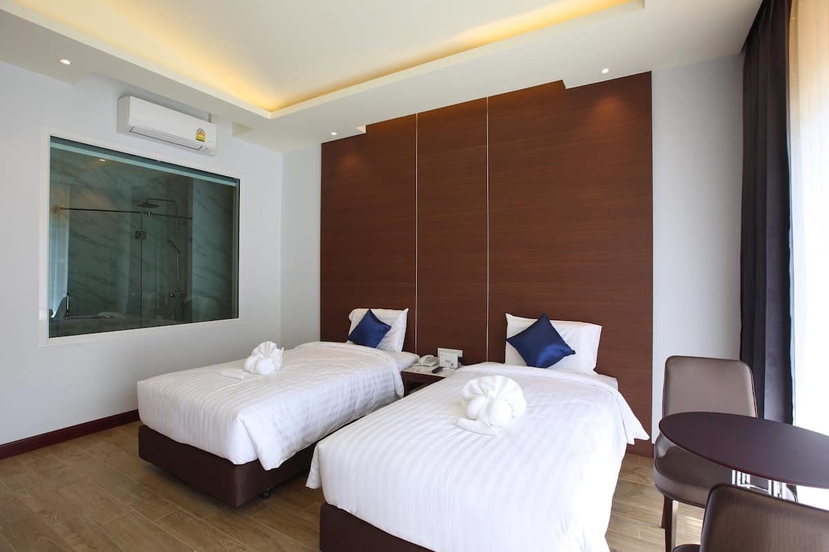 Een hotelkamer met twee bedden, een groot raam, een houten paneelwand, een tafeltje en een stoel.