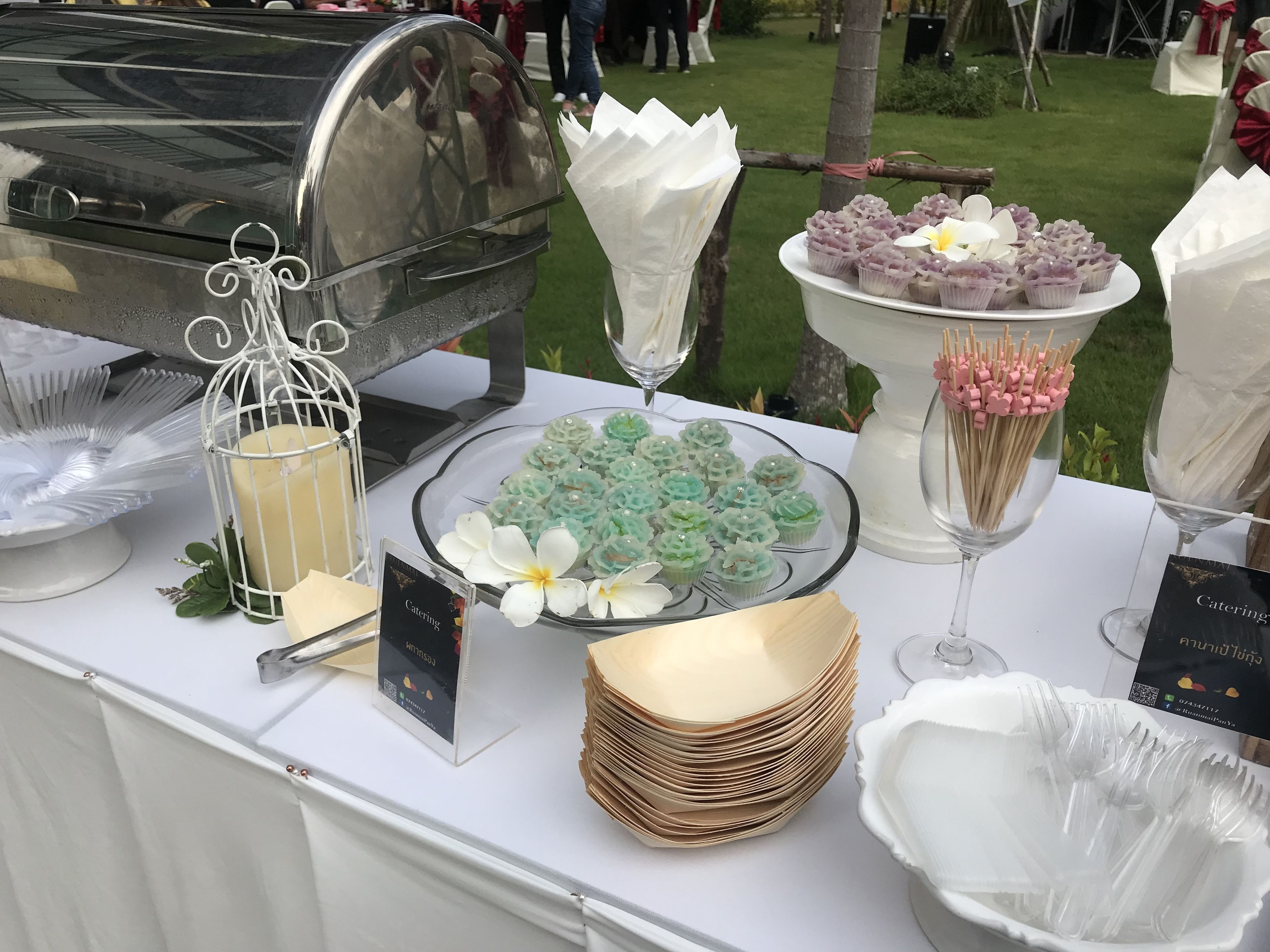 Een cateringtafel met diverse soorten eten, waaronder cupcakes, een kaars en een bordje waarop cateringdiensten worden aangegeven.