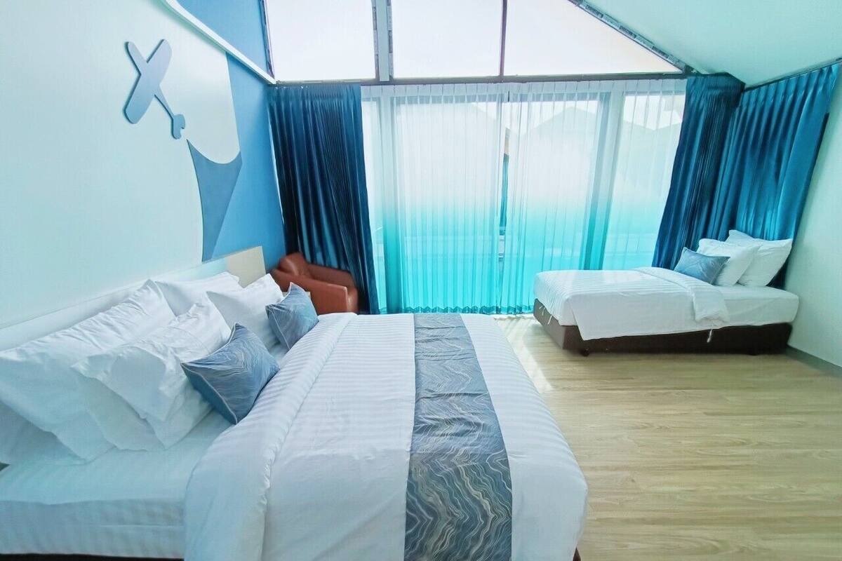 Een hotelkamer met twee bedden, een groot raam met gordijnen en een blauwe accentmuur.