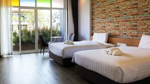 Une chambre d’hôtel avec deux lits, un mur décoratif en briques, une grande fenêtre donnant sur un espace verdoyant et une porte-fenêtre coulissante qui mène à un espace extérieur.