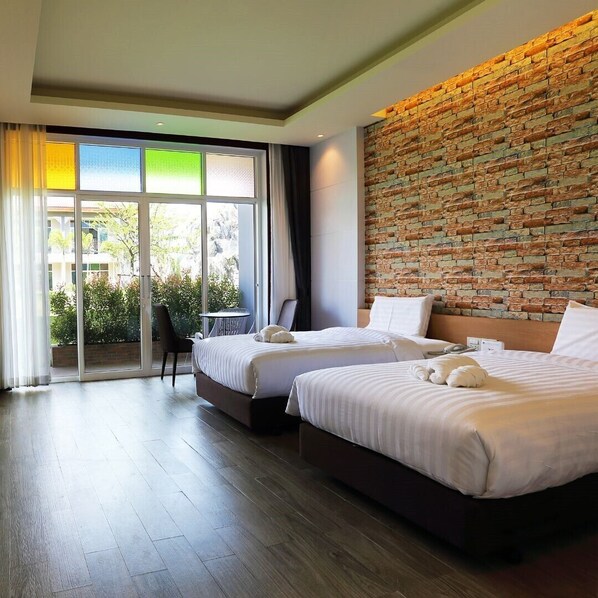 Une chambre d’hôtel avec deux lits, un mur décoratif en briques, une grande fenêtre donnant sur un espace verdoyant et une porte-fenêtre coulissante qui mène à un espace extérieur.