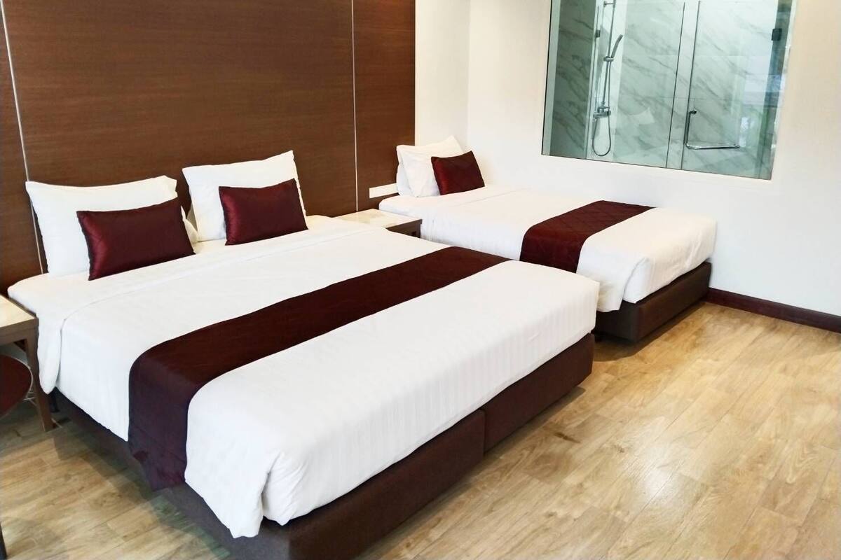 Een hotelkamer met twee bedden, een groot raam met uitzicht op een douche, en een houten vloer.