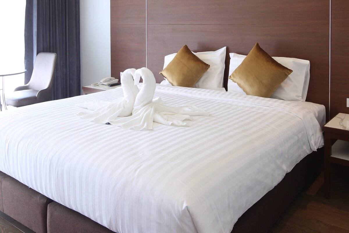 Een hotelkamer met een groot bed, een donker houten hoofdbord, witte beddengoed en twee bruine kussens.