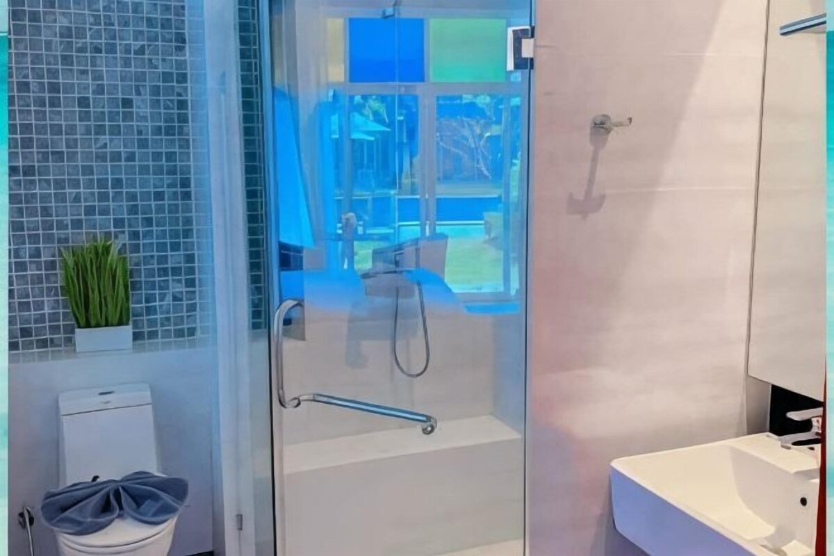 Un baño con cabina de ducha con puerta de vidrio, un lavamanos blanco y una pequeña planta en maceta.