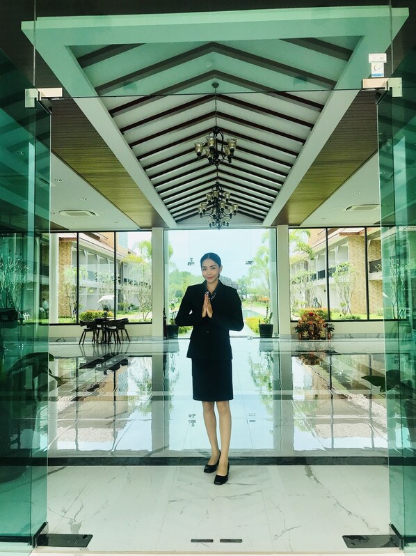 A person standing in a modern lobby with glass walls, a polished floor, and a geometric ceiling design.