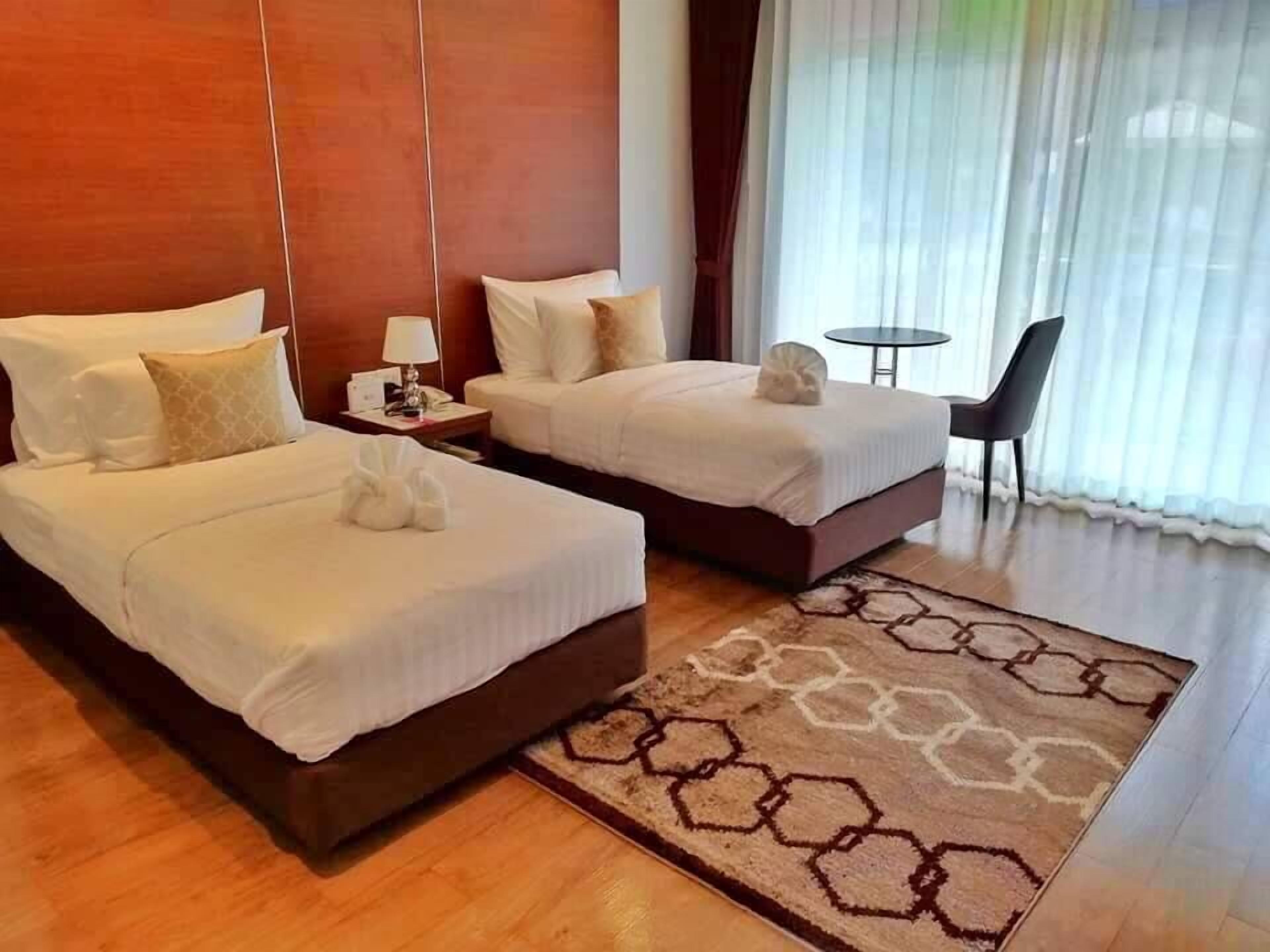 Ein Hotelzimmer mit zwei Betten, einem kleinen Tisch, einem Sessel und einem großen Fenster mit Vorhängen.