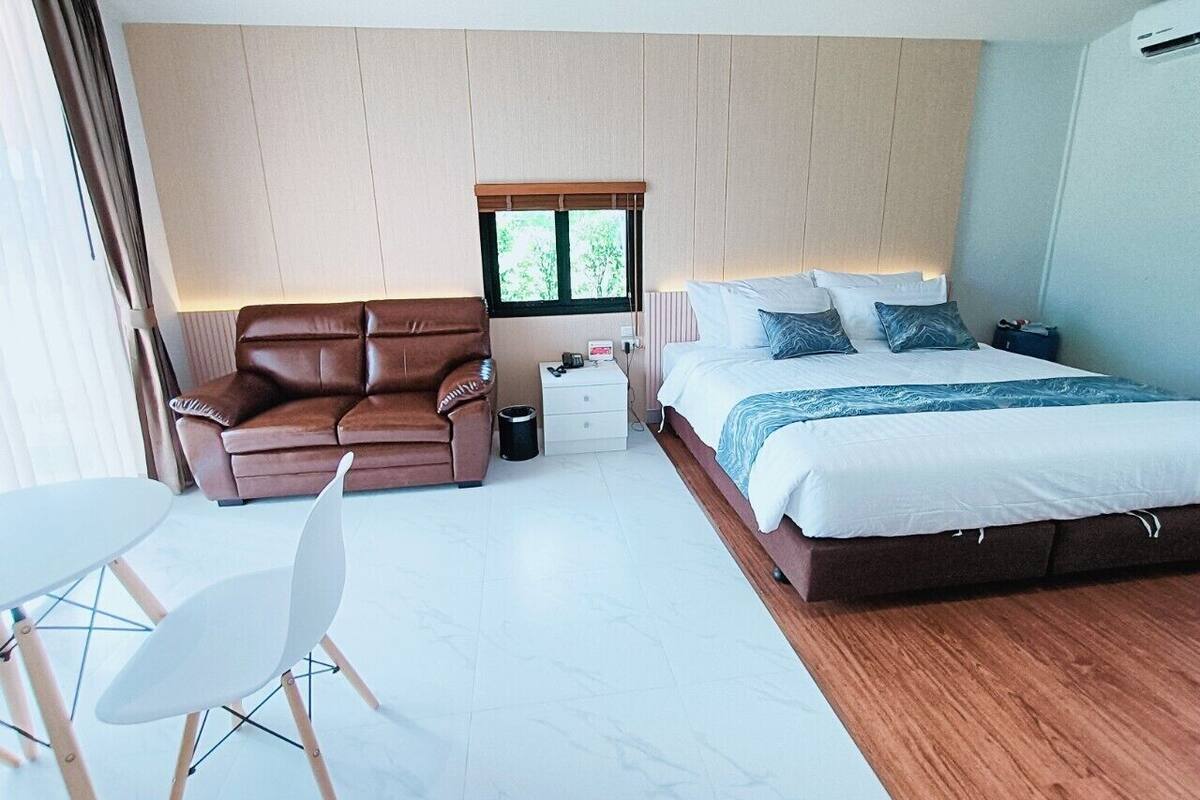 Een moderne hotelkamer met een groot bed, een bruine leren bank, een kleine tafel met stoelen en een raam met uitzicht op bomen.