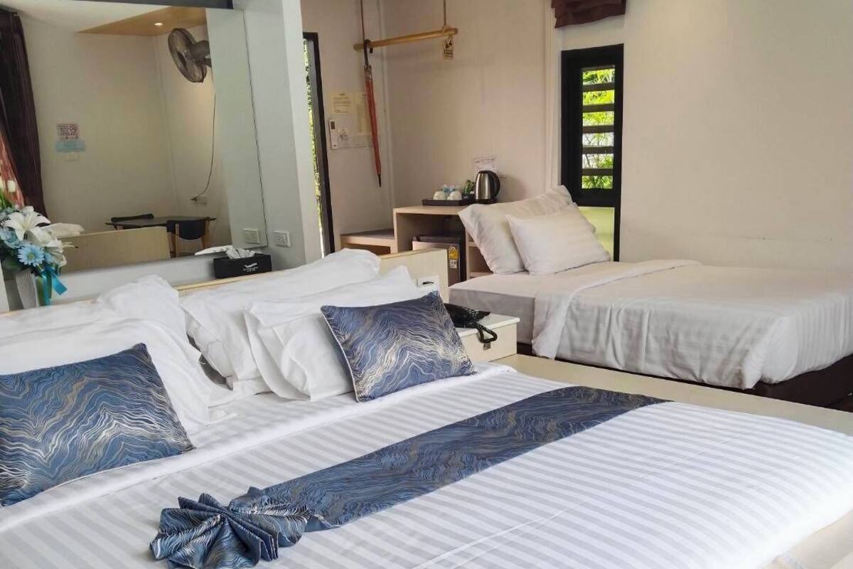 Hotelkamer met twee bedden, een bureau, een stoel, een spiegel en een raam met uitzicht op groen.