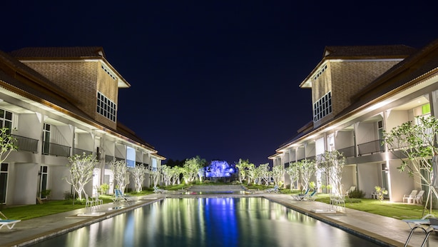 Vue nocturne d’un hôtel avec une piscine, des bâtiments à deux étages et une cascade en arrière-plan.