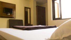 A neatly made bed with a white pillow and a folded brown blanket. A television is mounted on the wall above the bed. - Hotel Hill Town (Dharamshala)