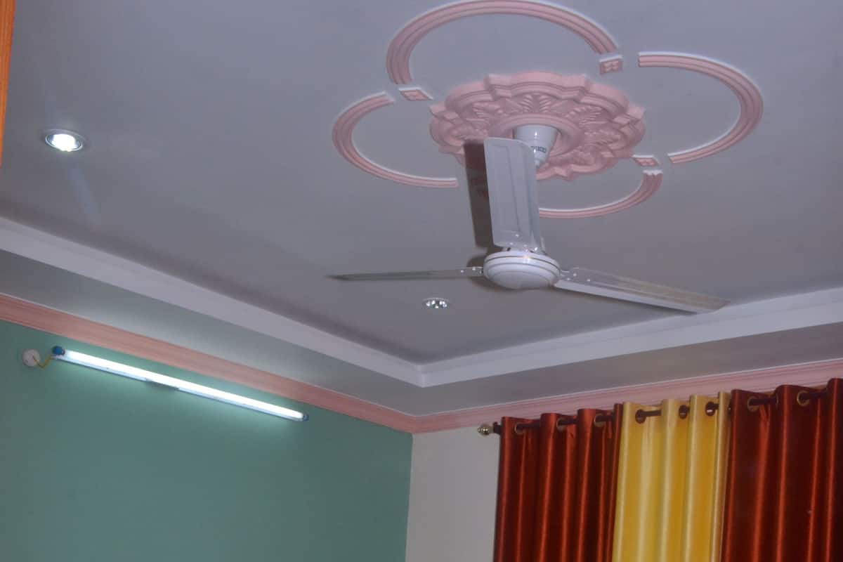 Una camera da letto con un letto di legno, una ventola a soffitto, un comodino e una finestra con tende rosse e gialle.