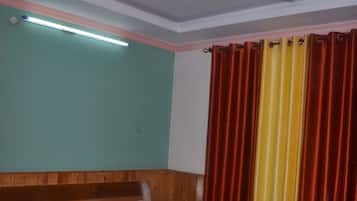 Un dormitorio con una cama de madera, un ventilador de techo, una mesita de noche y una ventana con cortinas rojas y amarillas.