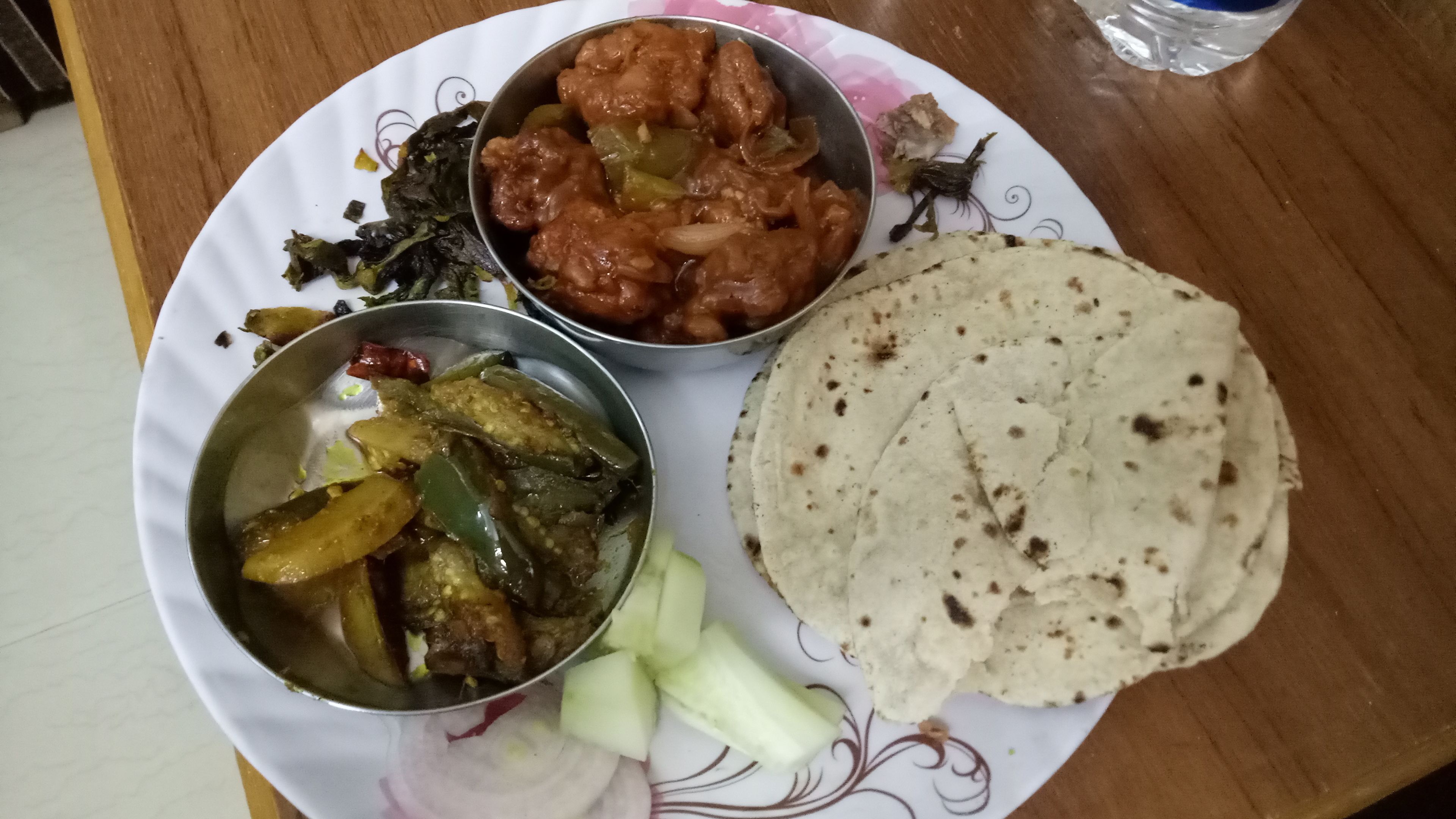 Un plato con una variedad de comidas, incluyendo un recipiente metálico con verduras, un recipiente metálico con carne y pan plano.