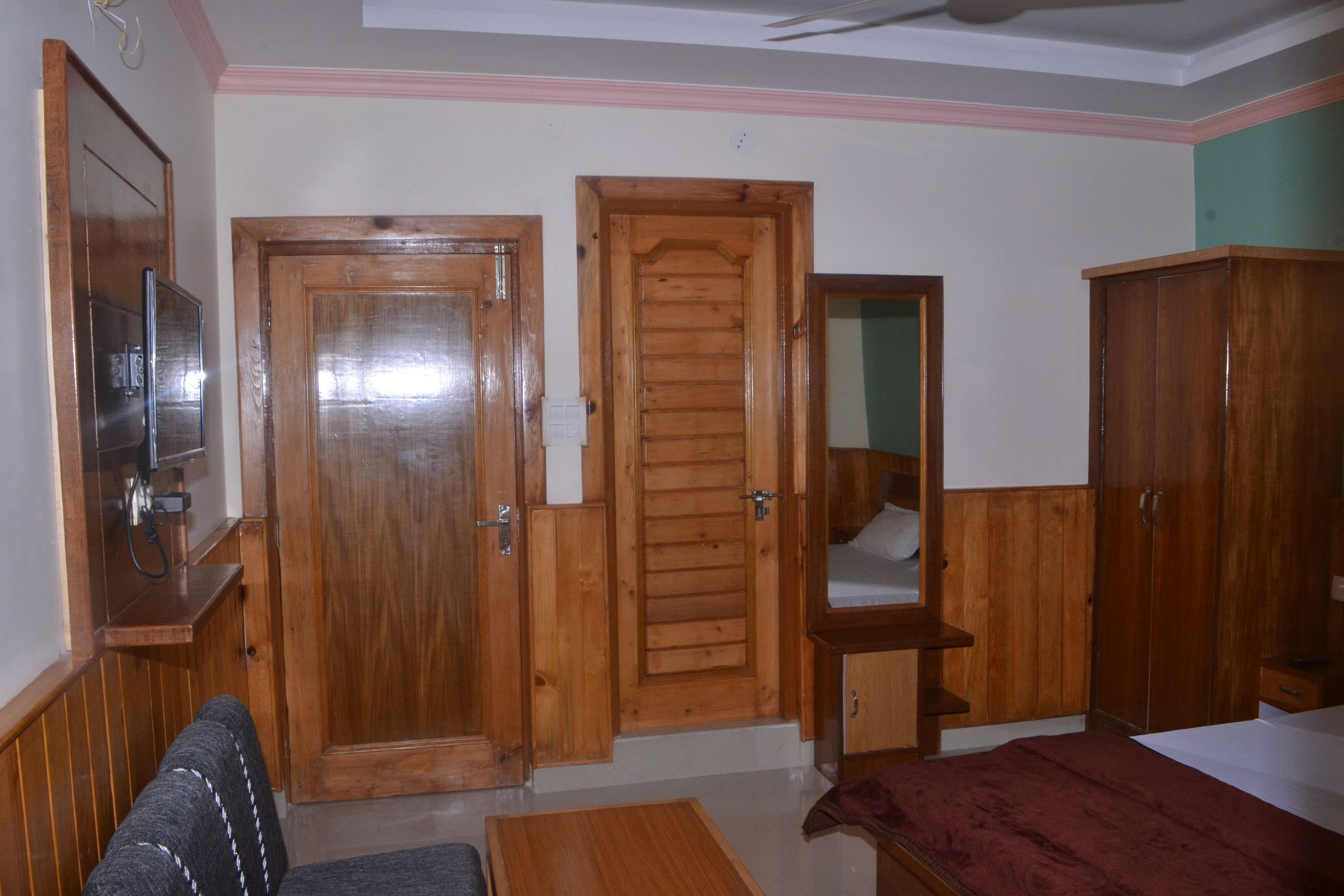 A bedroom with wooden doors, a bed, a small table, and a mirror.