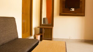 A room with a wooden cabinet, a television mounted on the wall, a sofa, and a small trash bin. - Hotel Hill Town (Dharamshala)