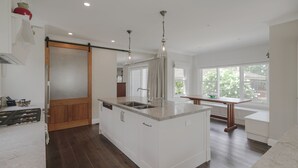A modern kitchen with a central island, wooden flooring, and a sliding door leading to another room. - Cherrywood - Luxury retreat - with complimentary EV charging (Exeter)